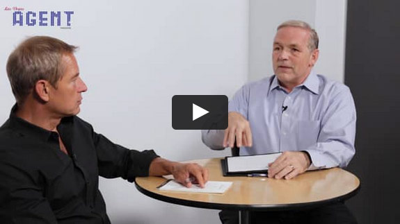 Two men sit at a round table, discussing. One holds a notepad. AGENT is at top left. A play button signals a trust lawyer video.