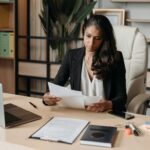 A woman in business attire reviews Financial Crimes Enforcement Network documents at her desk, with office items and plants nearby. A woman in business attire reviews Financial Crimes Enforcement Network documents at her desk, with office items and plants nearby.